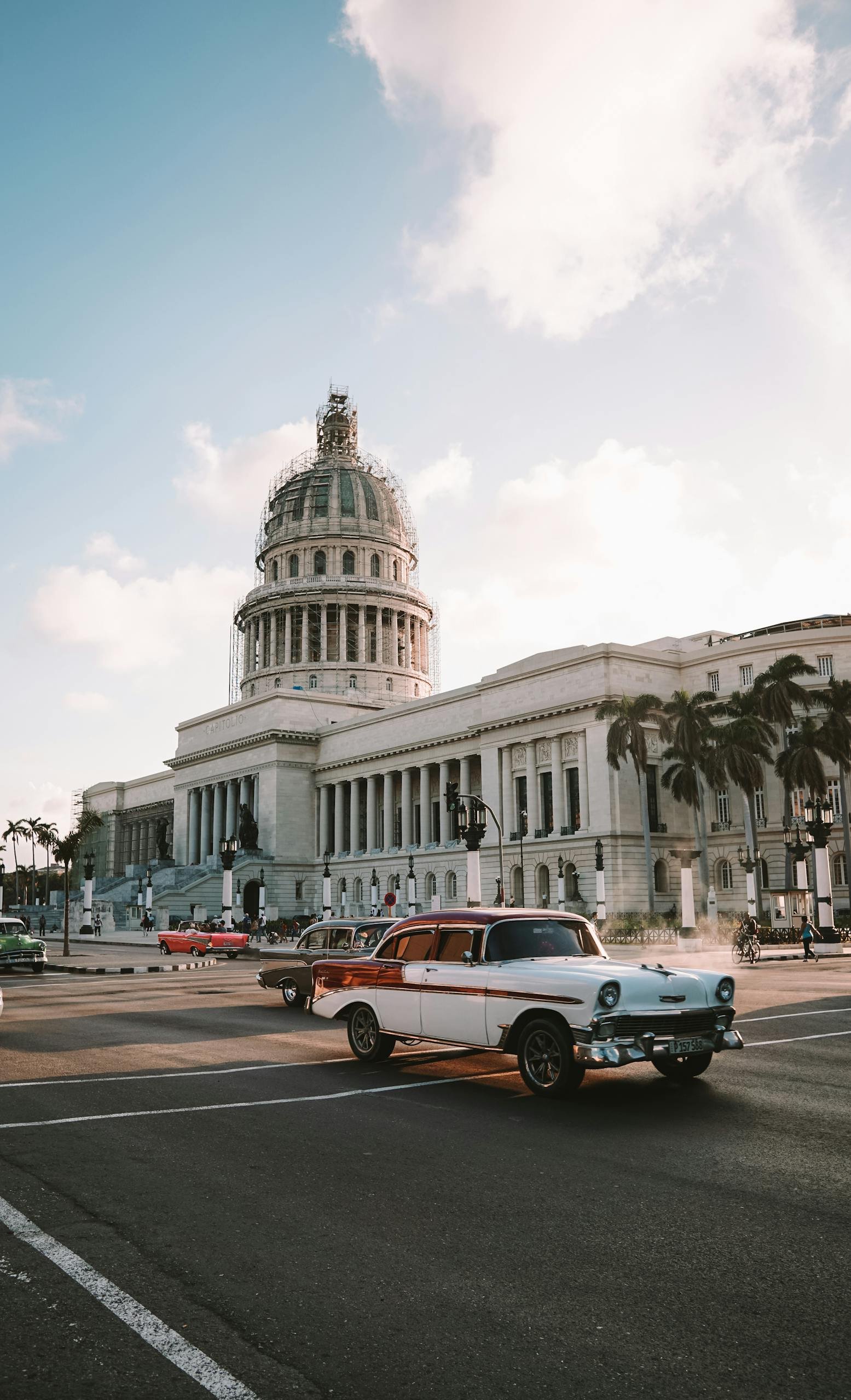 Vintage car driving past El Capitolio in Havana, showcasing Cuban architecture.