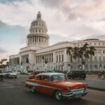 A classic car drives past the historic El Capitolio in Havana, Cuba, under a dramatic sky.