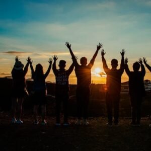A diverse group of friends raises their arms in celebration against a vibrant sunset backdrop.