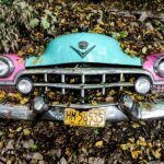Front view of a classic car covered in autumn leaves, showcasing vintage design.